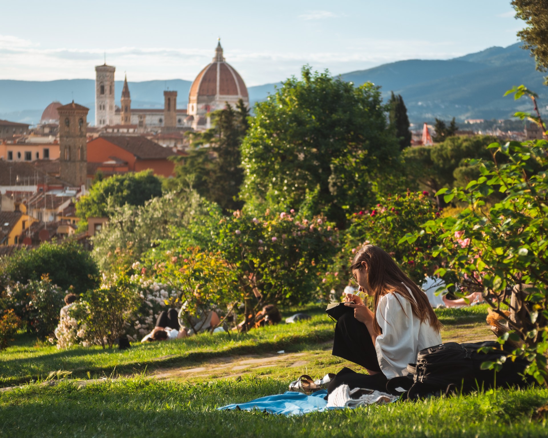 Junge Frau liest im Gras, im Hintergrund Florenz